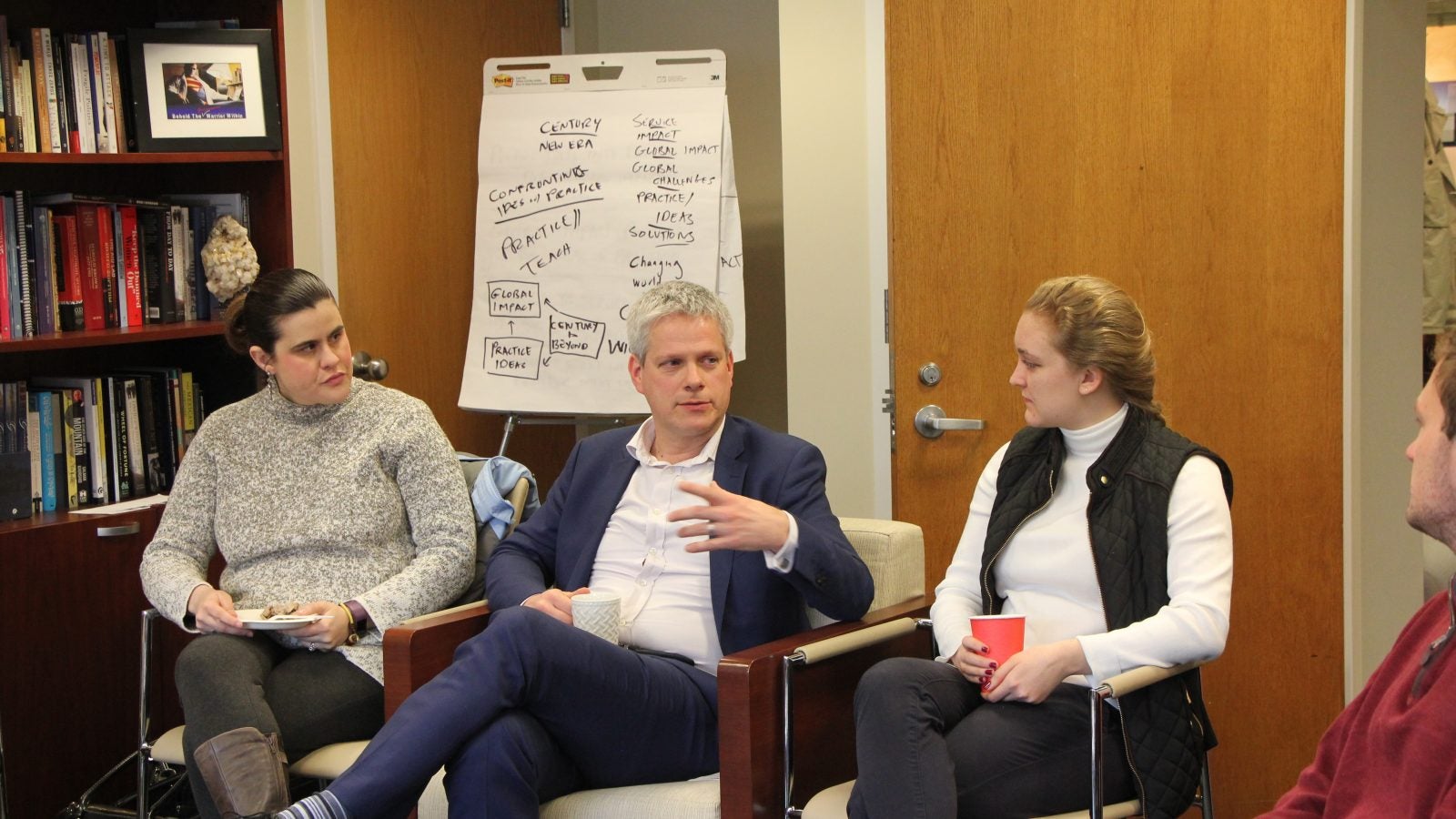 People in chairs have conversation in office.