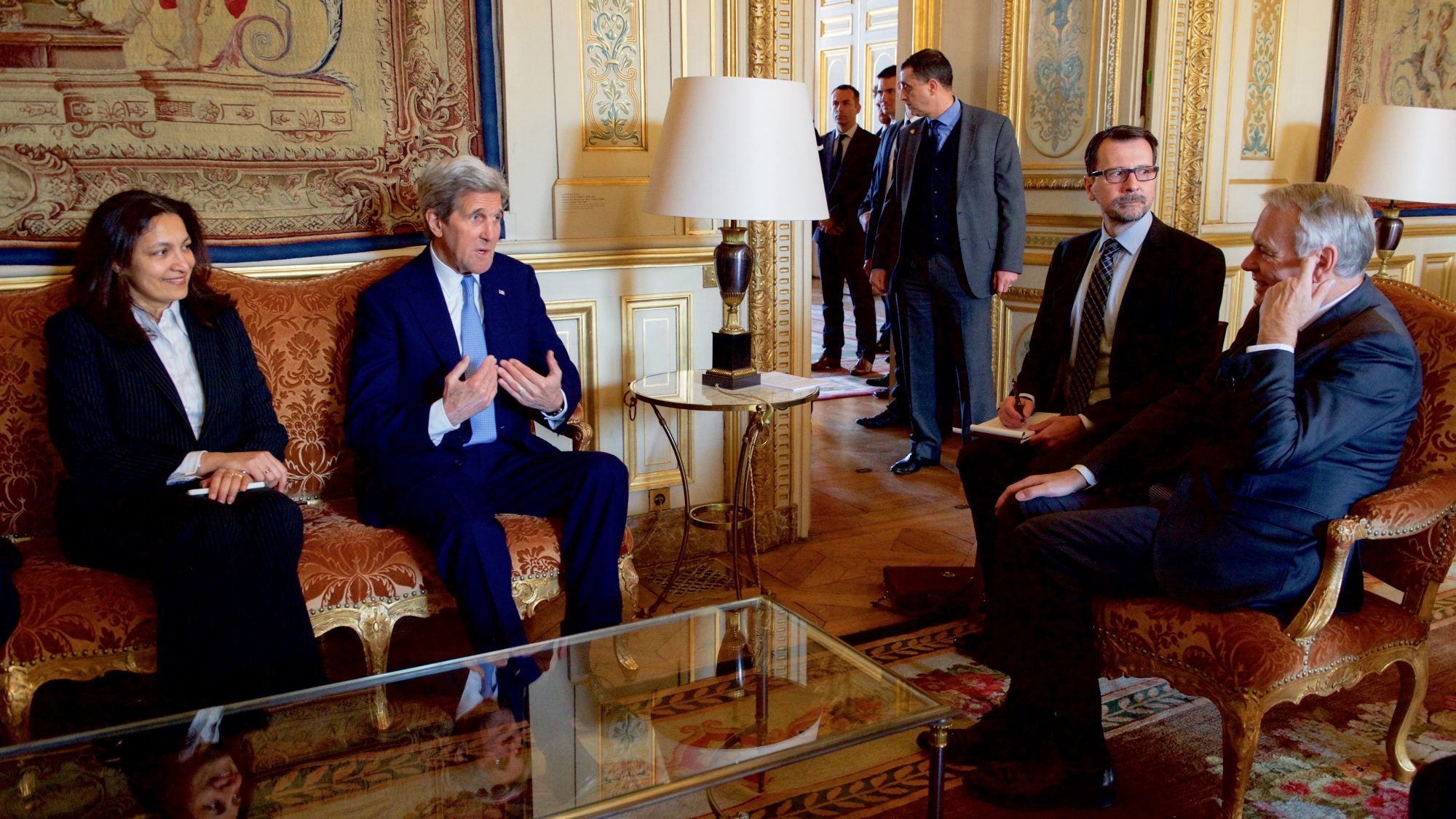 Men and women sit around a table in a well-furnished room.
