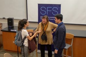 Three people talk at the front of a room.