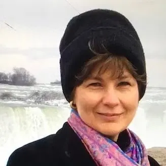 Headshot of Paula Doyle wearing a black knit hat, pink scarf, and black wool coat.