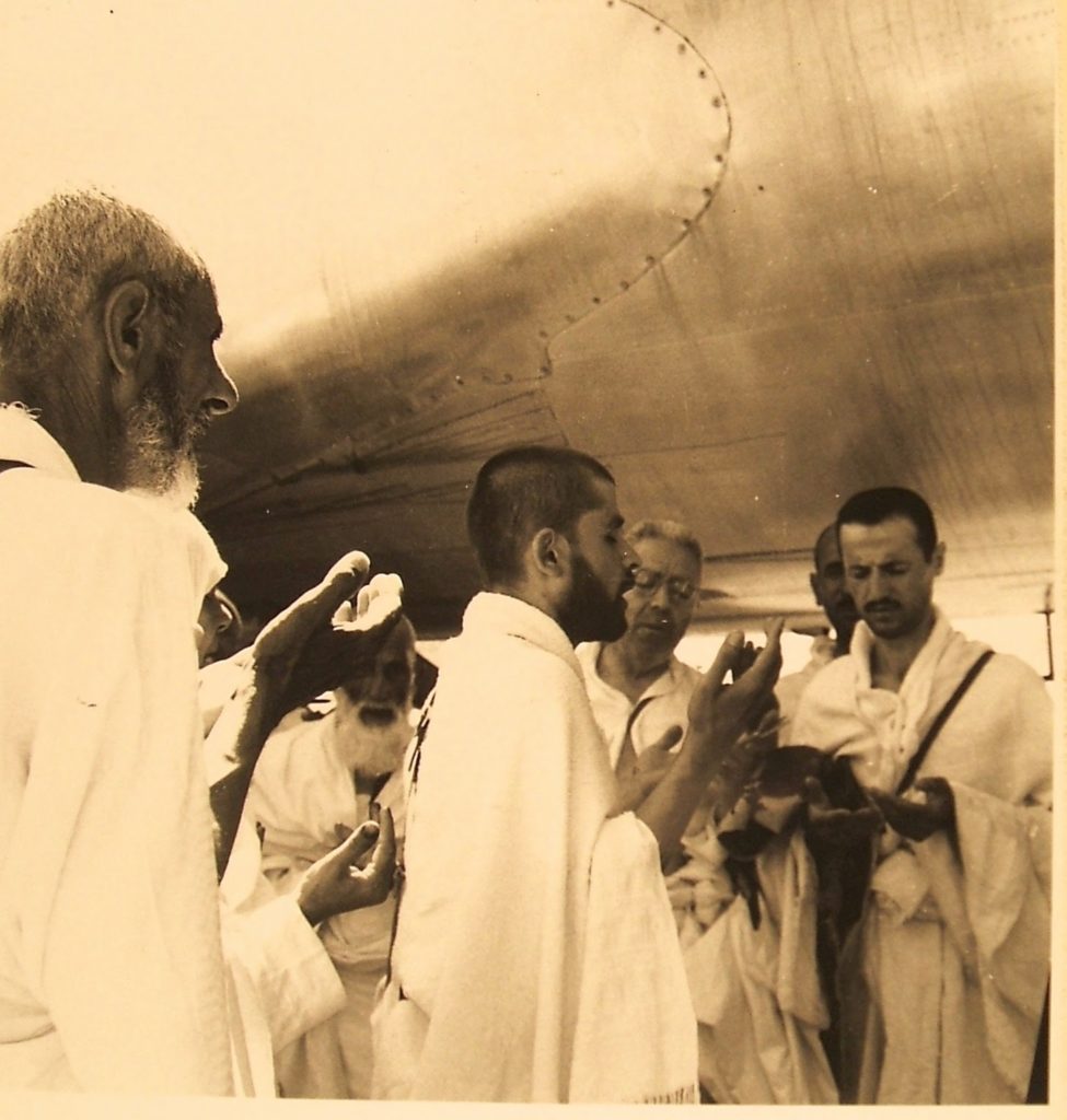 Men in robes praying to allah underneath airplane