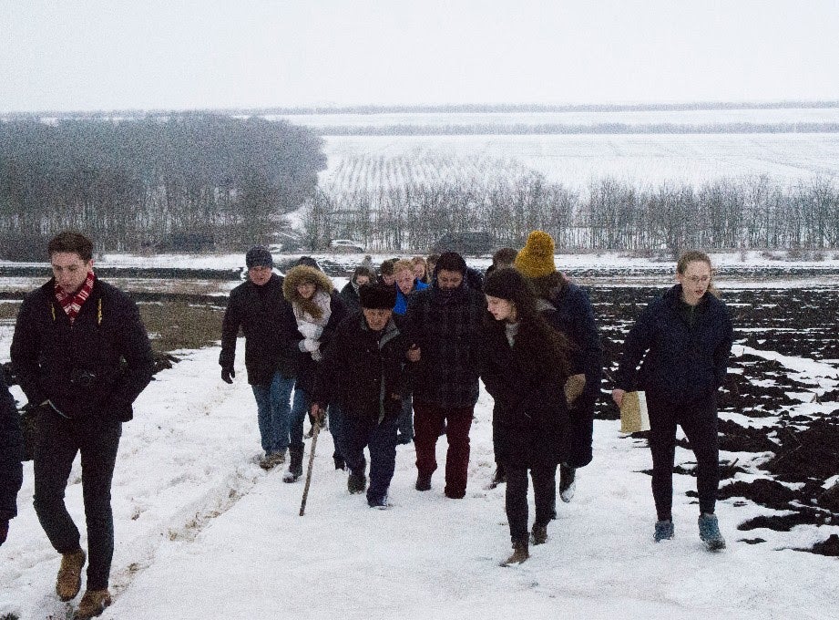 Group of people walk through snowy field.