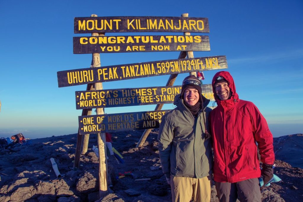 Two people stand at the top of Mount Kilimanjaro.