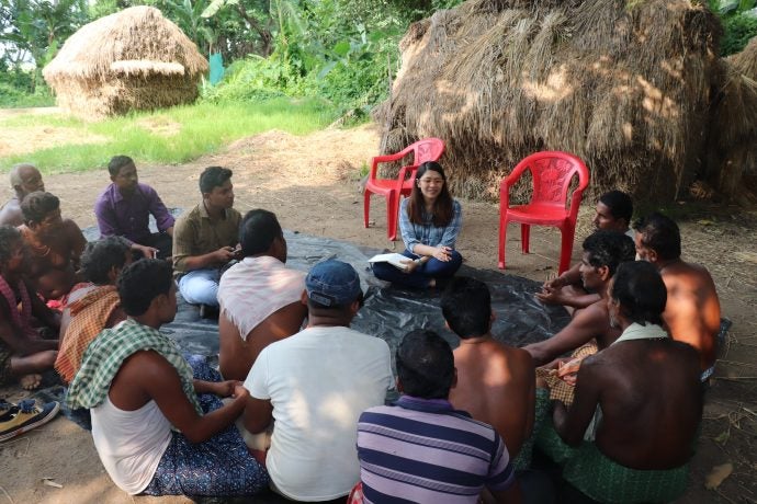 Woman interviews group of farmers while seated.