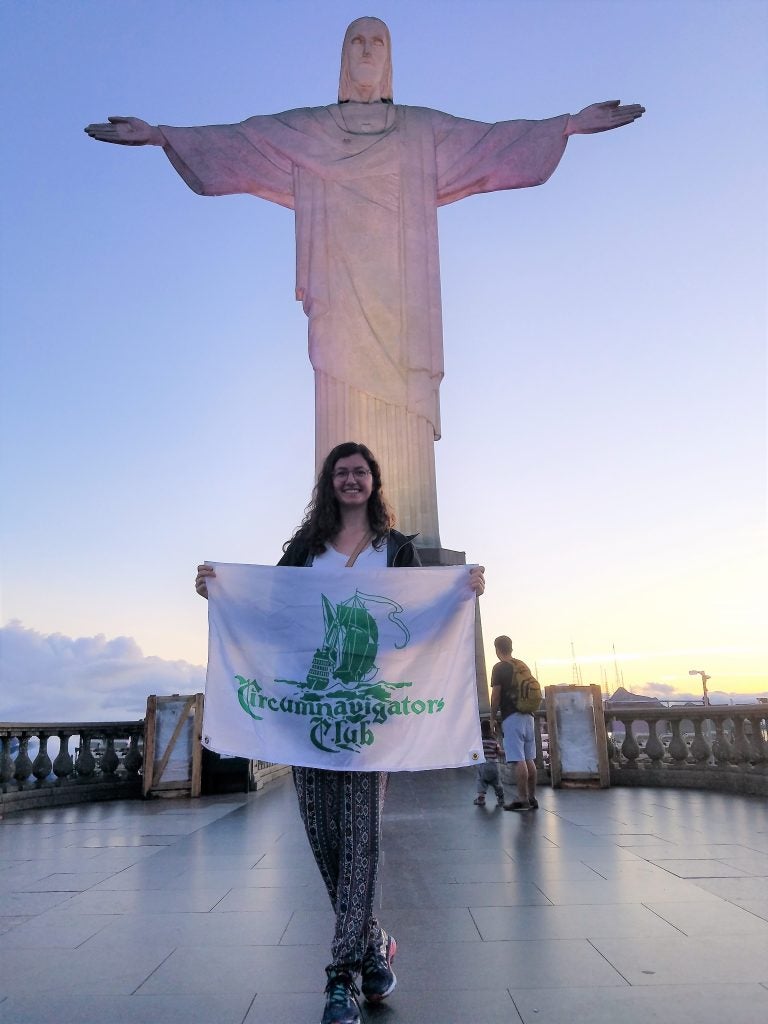 Woman poses holding flag in front of statue.