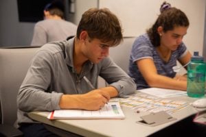 Student takes notes while sitting next to another student at table.