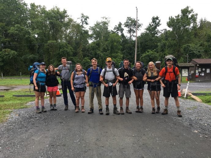 Group of ten people with backpacks and camping gear pose for a photo outside.