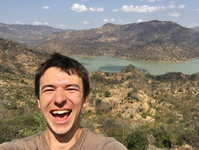 Smiling man takes a selfie in front of mountains.