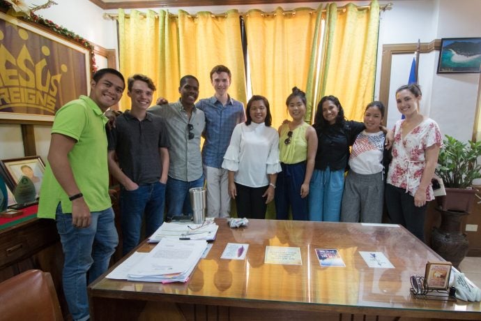 Group of nine people pose for a photo around a table indoors.