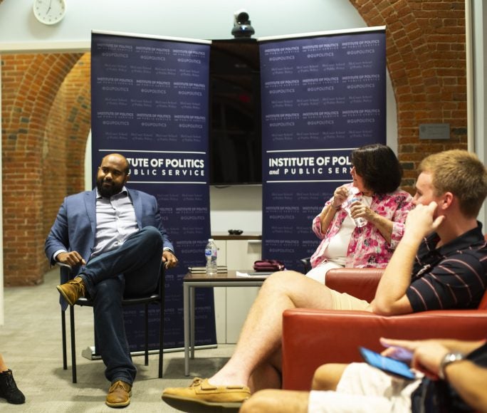 People seated in chairs in circle listen to man.