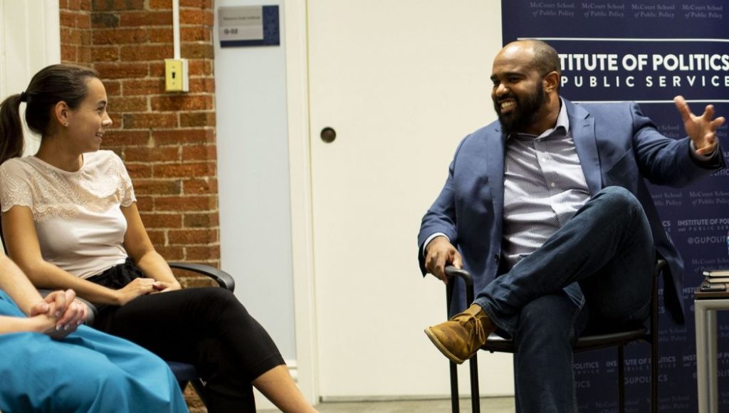 Man and woman talk in chairs in larger circle of people.