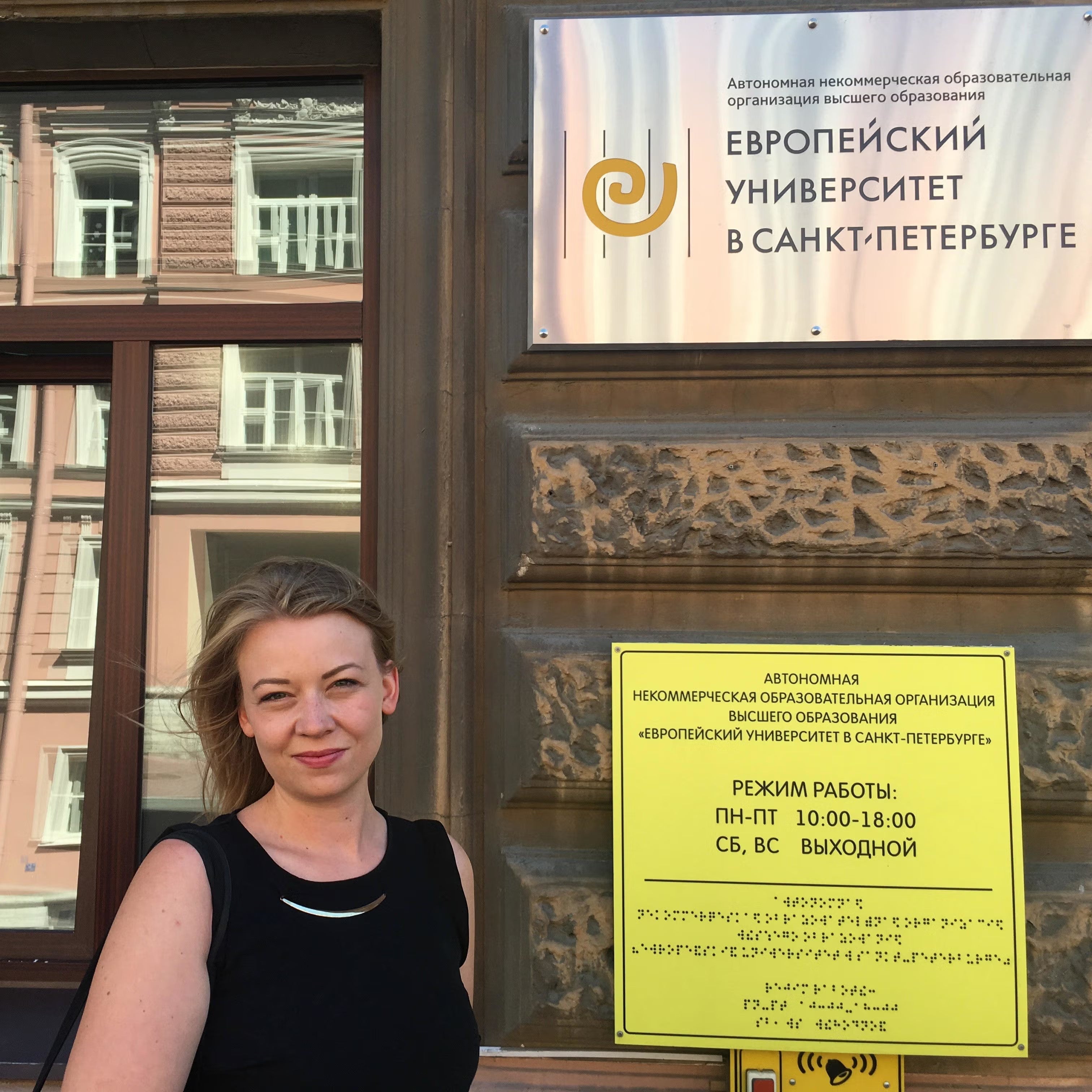 Iida Tikka in Russia, standing near environmental notice, wearing black sleeveless top.