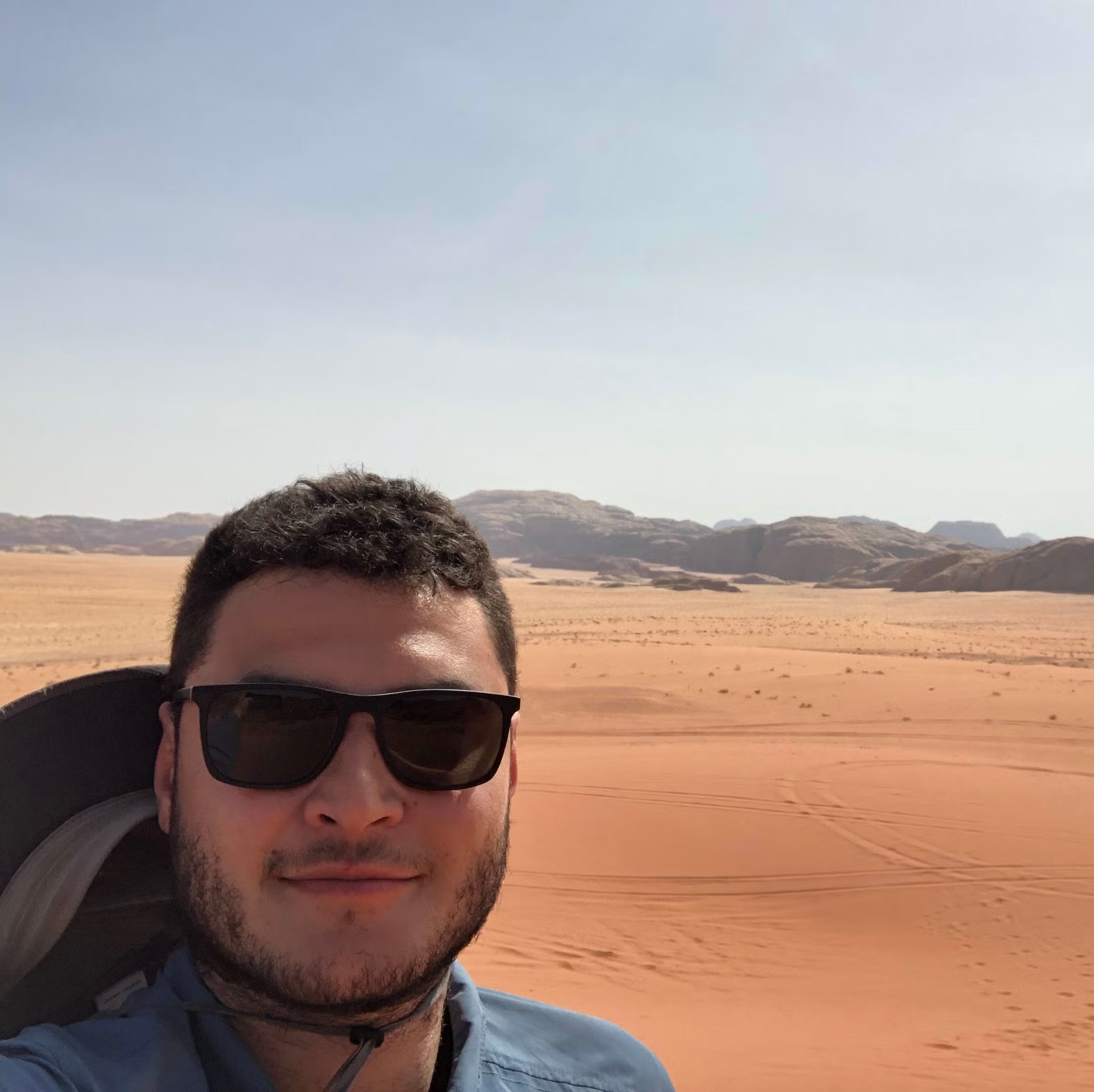 Yuri Neves wearing dark sunglasses, in a blue t-shirt standing in a desert.