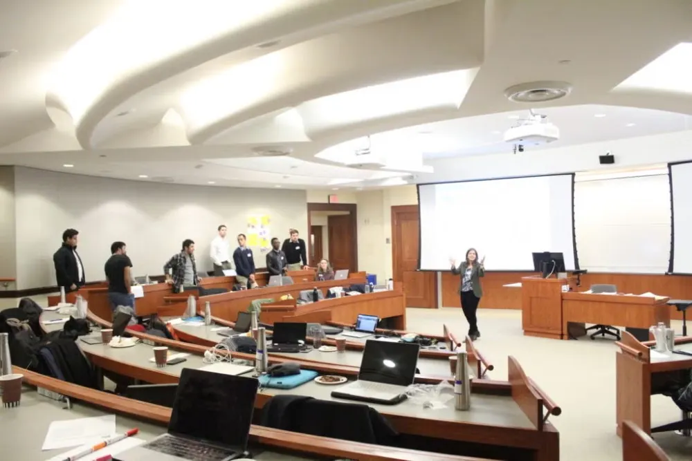 Students are standing in classroom listening to a woman speak during the Social Innovation Lab competition.