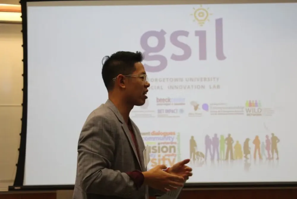 Young man in glasses and gray sweater speaks during Social Innovation Lab competition.