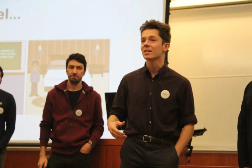 Young man in navy blue long-sleeve button down shirt and dark slacks presents with team during Social Innovation Lab competition.