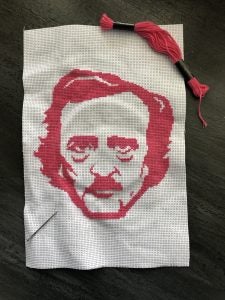 Photo of pink cross-stitch of Edgar Allen Poe. 