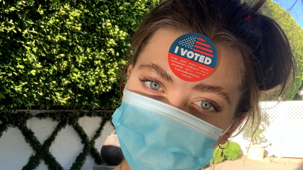 Amelie Zilber is pictured wearing a face mask and has an "I voted" sticker stuck on her forehead.