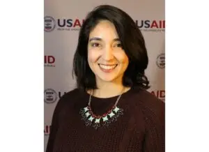 Young woman with dark brown hair in dark brown sweater wearing turquoise, red, and navy statement necklace