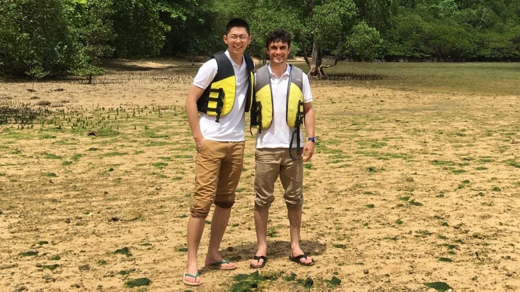 Briant Britt is pictured with a friend. They are on a sandy, grassy beach and wearing life jackets.