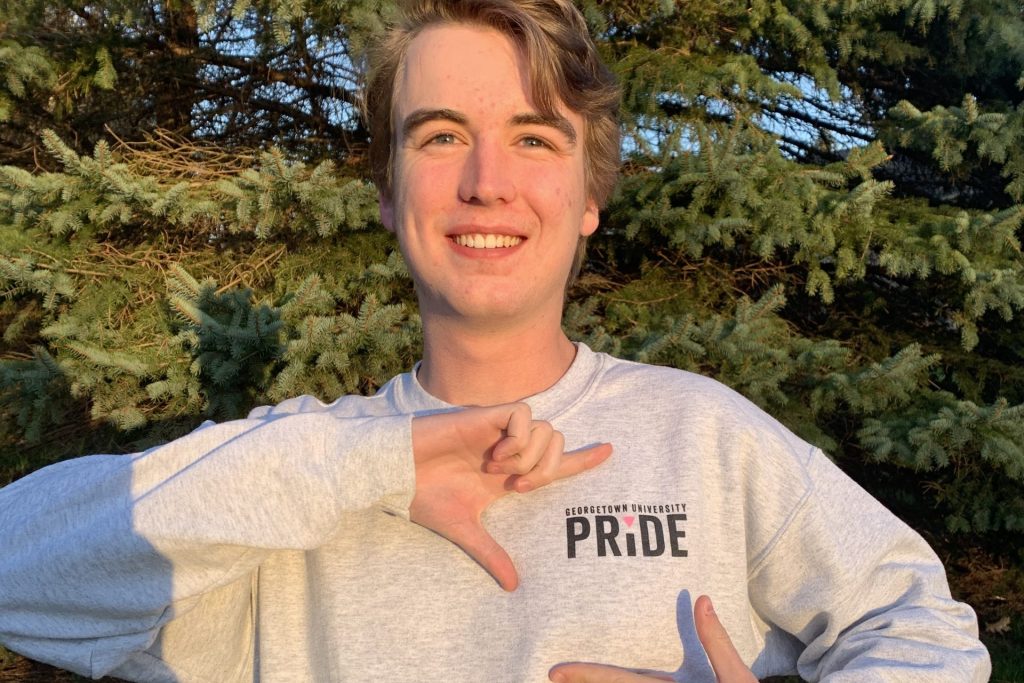 Failor wears a GU Pride sweatshirt, framing the club's logo with his hands.