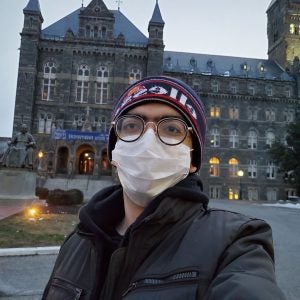 A selfie of Costantin in the early morning in front of Healy Hall. He is wearing a mask and a winter hat.