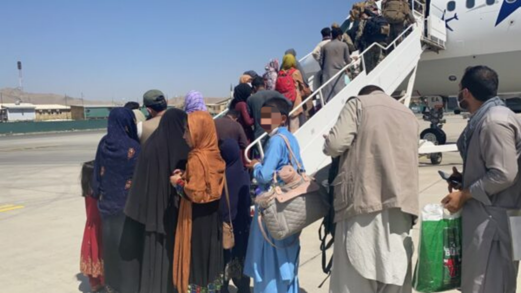 Afghans line up to board a plane. The face of a person facing the camera is pixelated to protect his identity.