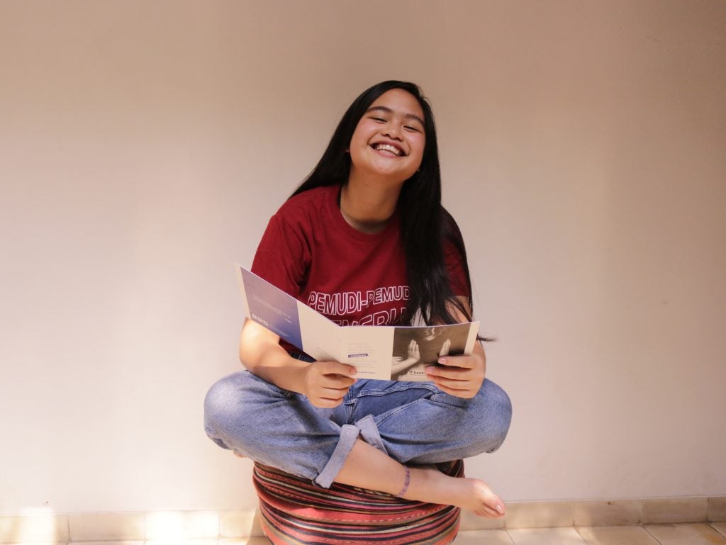 Photo of Faye Simanjuntak sitting cross-legged and smiling.