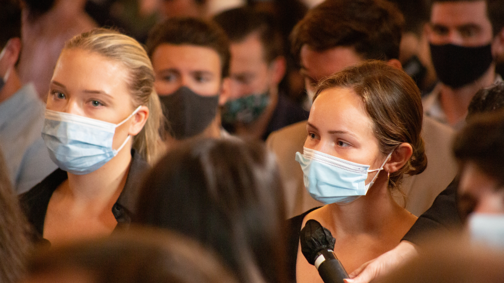 Female student wearing face mask speaks into a microphone.