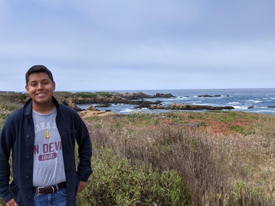 Photo of Tristin Sam (SFS'23) smiling while standing next to a coastline.