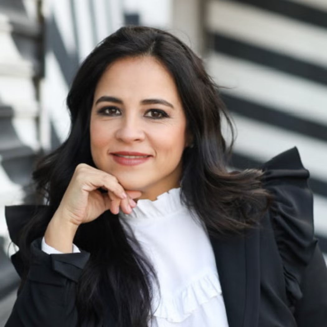 Headshot of Pilar Guzman Zavala, with hand resting on chin, wearing black blazer and white top.