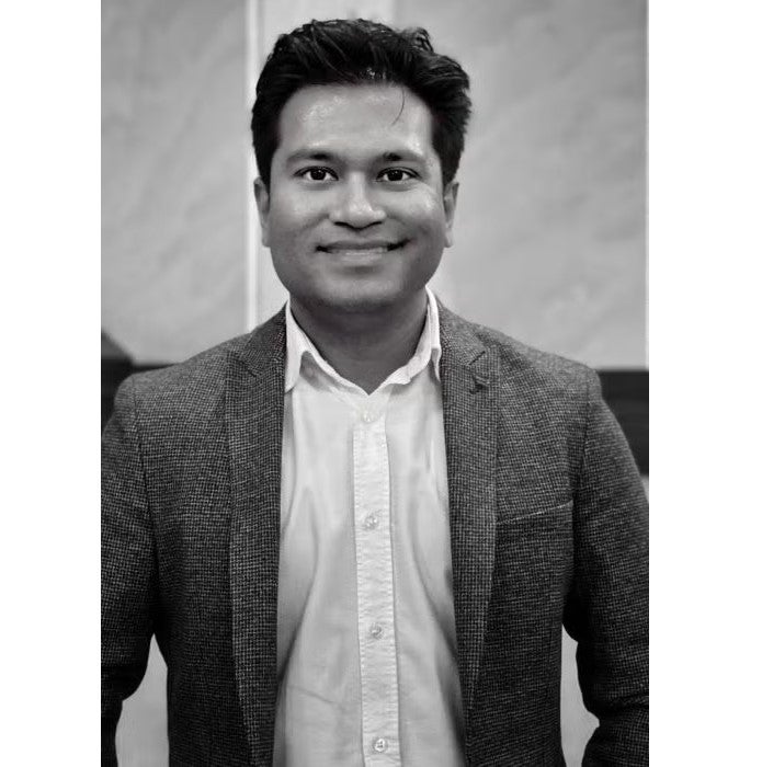 Young man standing in light button down shirt and dark blazer
