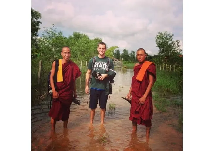 Brendon Thomas in dark t-shirt and dark shorts standing with two religious dignitaries.