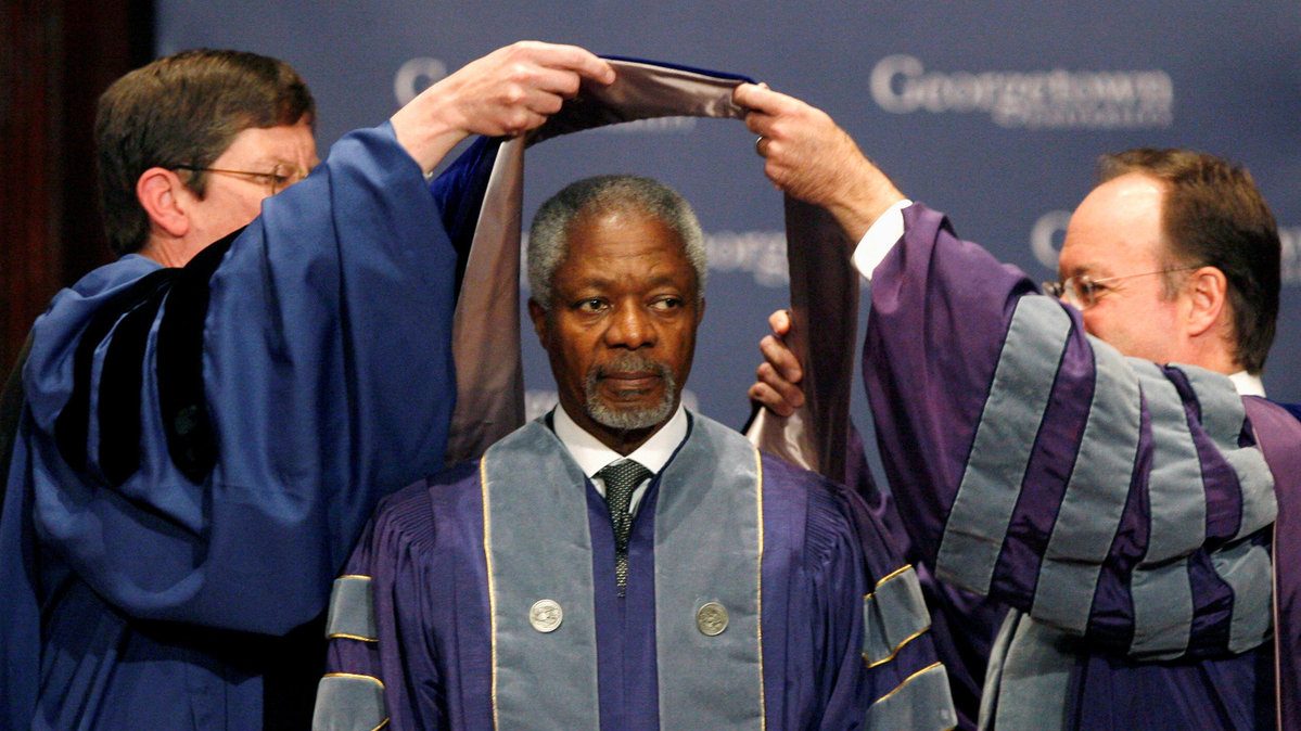 Kofi Annan, in Georgetown academic robes, is "doffed" with an academic cap by Georgetown President John DeGioa and another man.