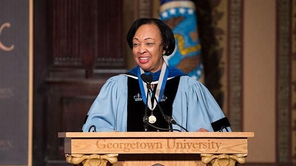 Mikell speaks from behind podium wearing her academic regalia