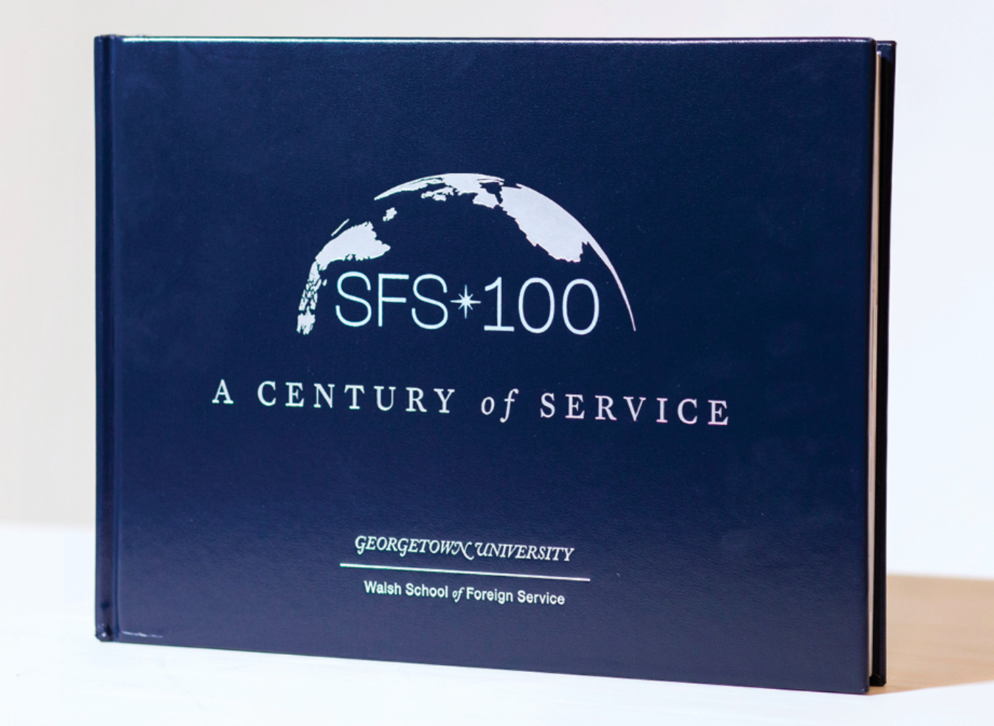 A staged photo of the SFS 100 book. It has a simple dark blue cover with a half globe on it, as well as the title, SFS 100: A Century of Service.