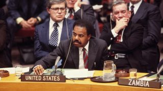 A photo of U.S. Ambassador to the UN Donald F. McHenry (PHD'63) sitting behind a desk with a microphone and a 