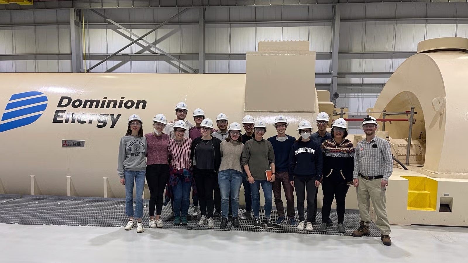 A group of students in casualwear and white hardhats standing in Dominion Energy facility.