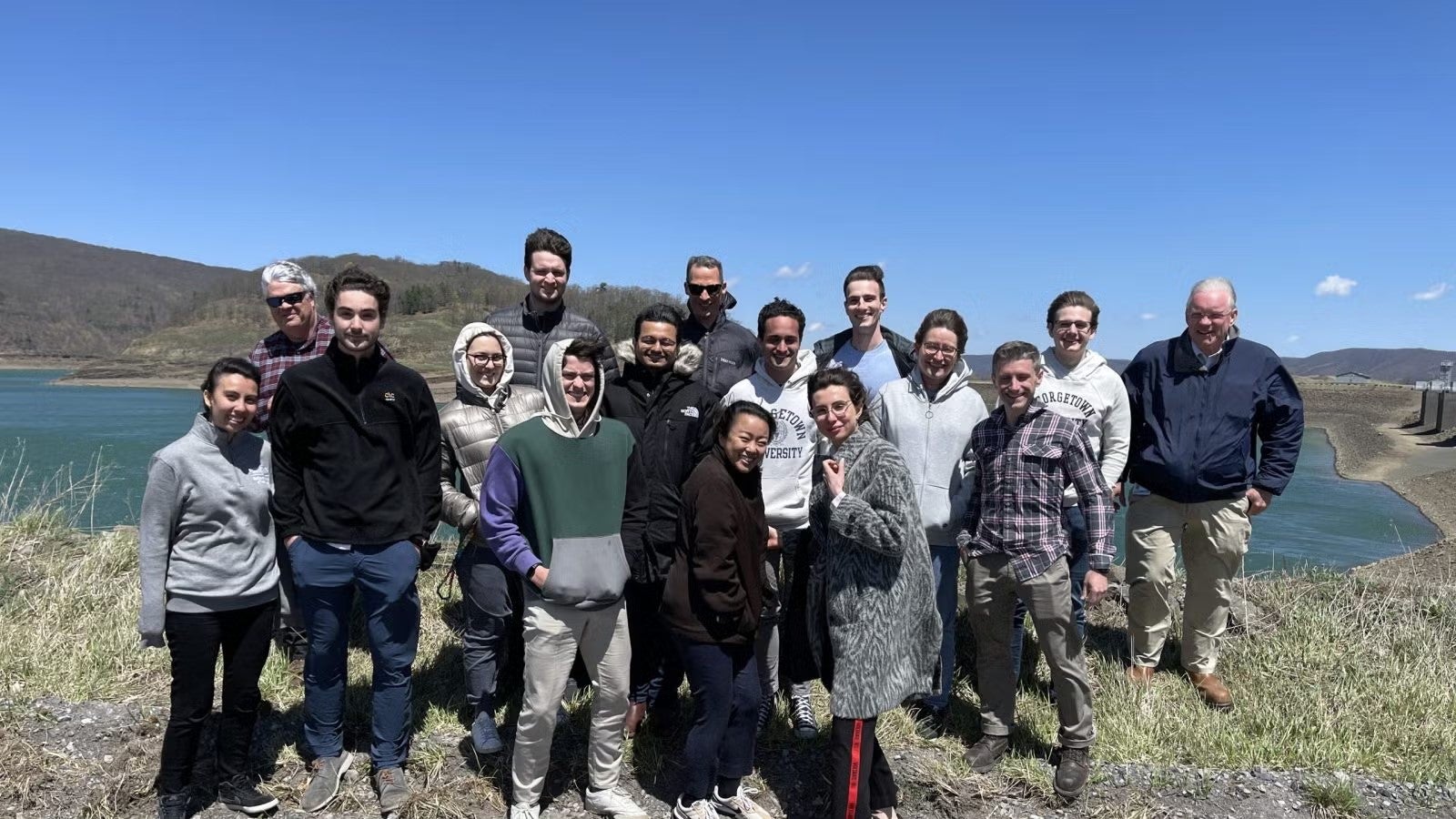Group of students standing together in casualwear outside, near reservoir.