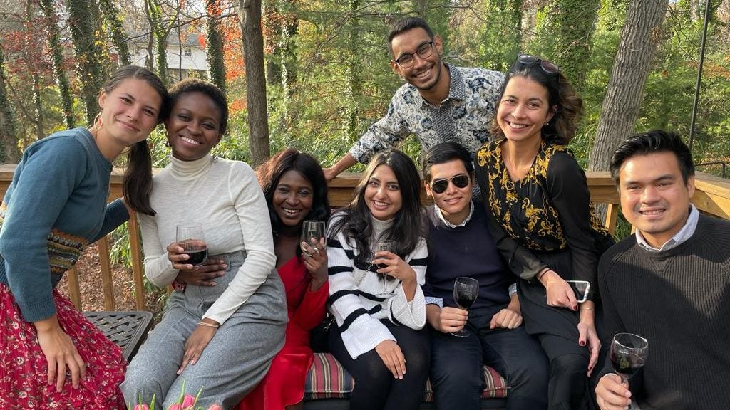 Alesh poses with friends in a garden. They hold glasses of wine. 