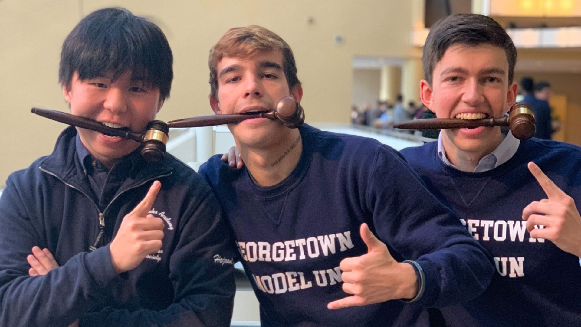 A photo of Kim and two friends. All three of them are wearing Georgetown Model United Nations sweatshirt and smiling with gavels between their teeth.