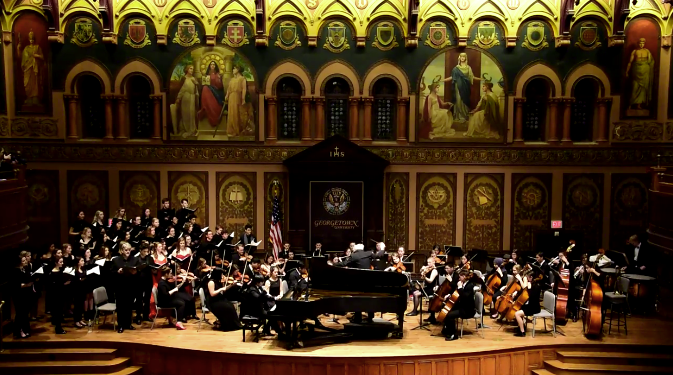 A photo of a student orchestra playing on stage in Gaston Hall