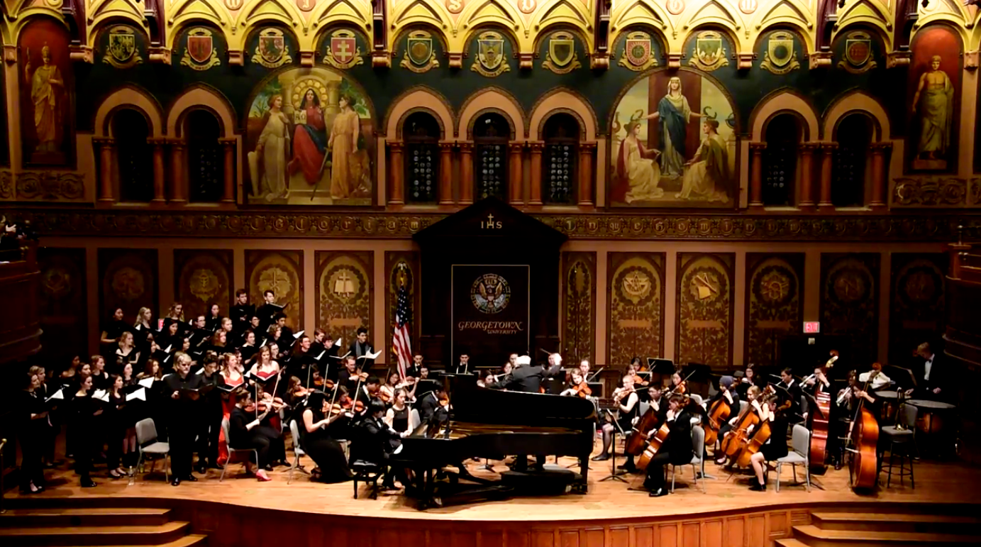 A photo of a student orchestra playing on stage in Gaston Hall