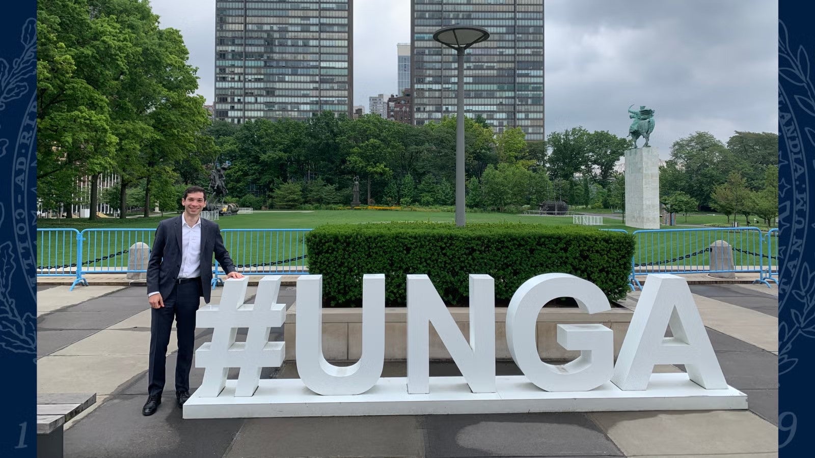 Caleb Diamond standing in front of '#UNGA' sign, wearing a navy blue suit and white shirt.