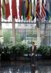 Joyce Yang poses for a photo in a hallway with world flags hanging around her