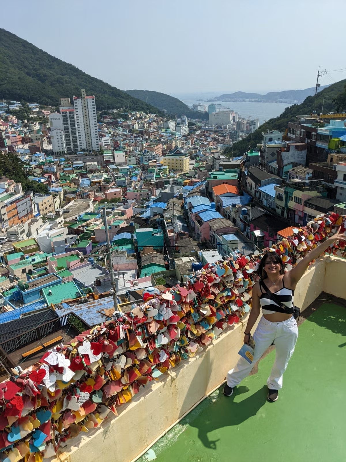 Kavya Sankhavaram in front of houses and mountainside, wearing a black and white striped top and white pants.