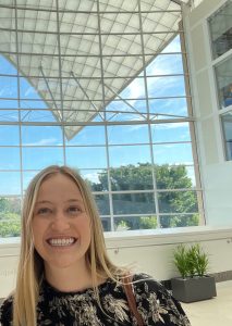 Lily Erickson takes a selfie in an atrium in front of a large window