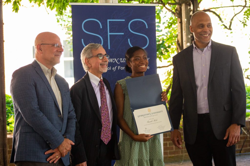 Dean Hellman, Professor Arend and Scott Taylor pose with a participant in front of an SFS banner 