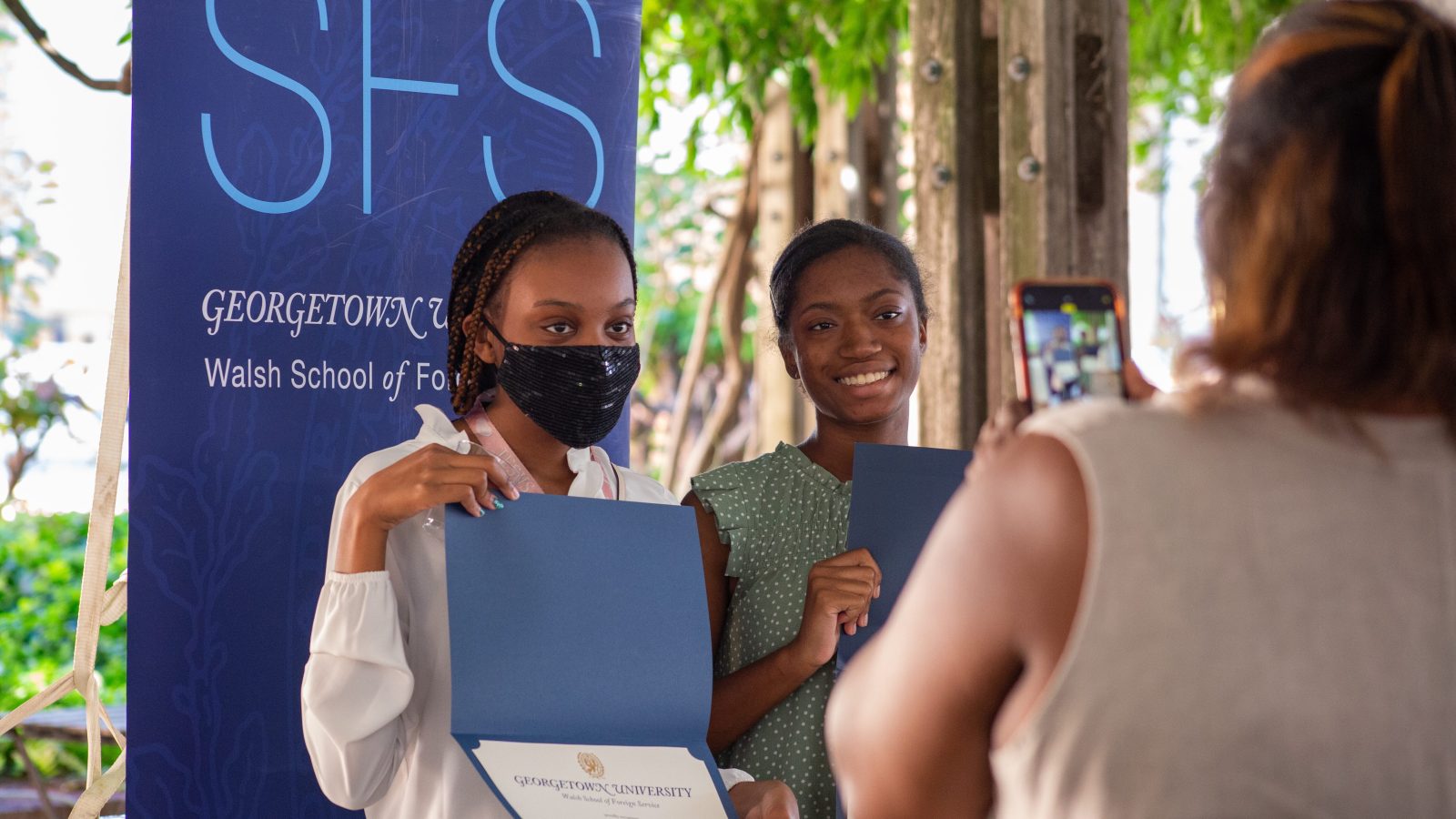 Two masked students pose with certificates in front of SFS