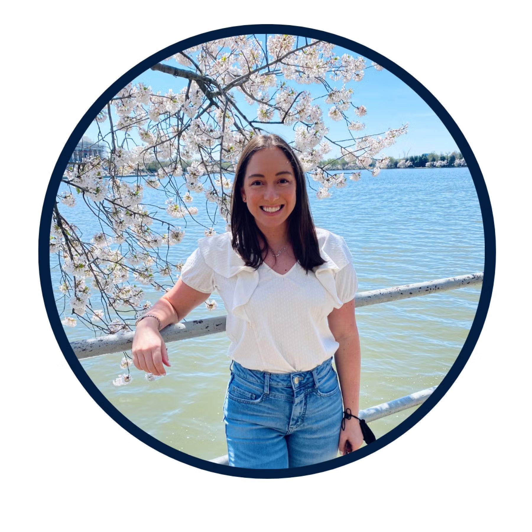 Megan Collins Headshot standing by cherry blossom tree in white blouse and light denim jeans.
